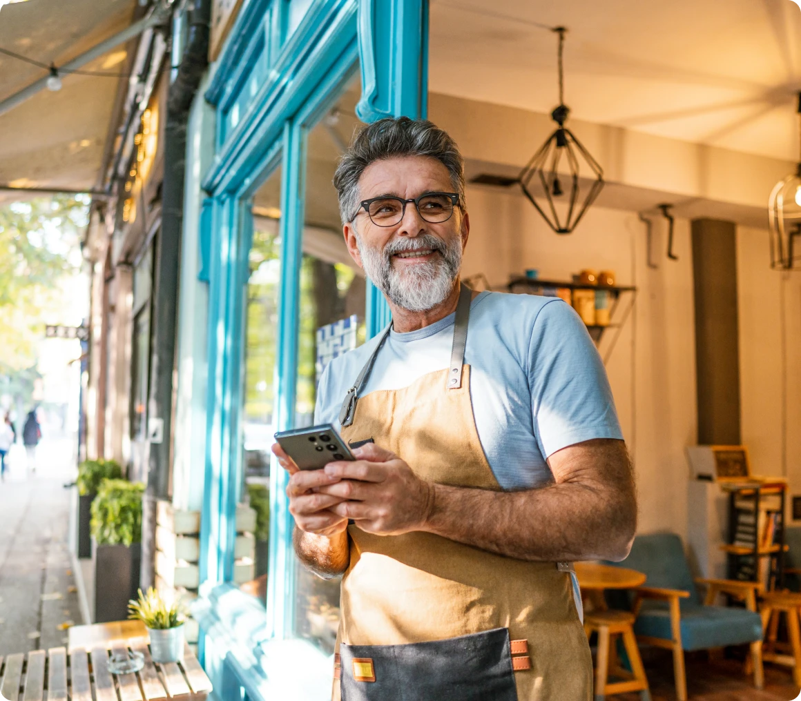 Man in apron smiling outside a café.