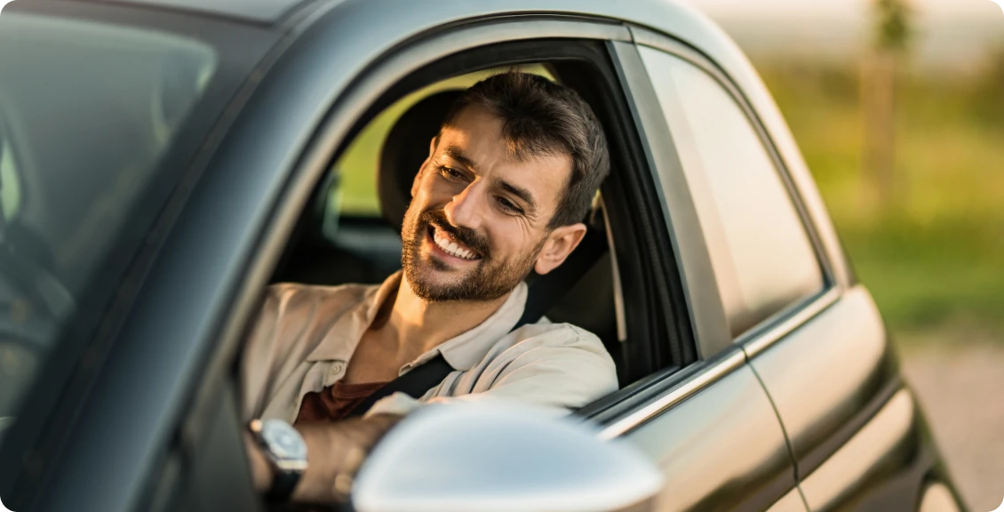 Smiling man driving car on sunny day.