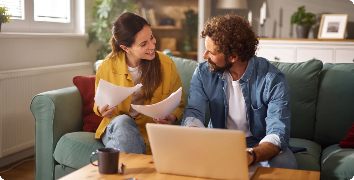 Couple smiling, discussing papers on couch.